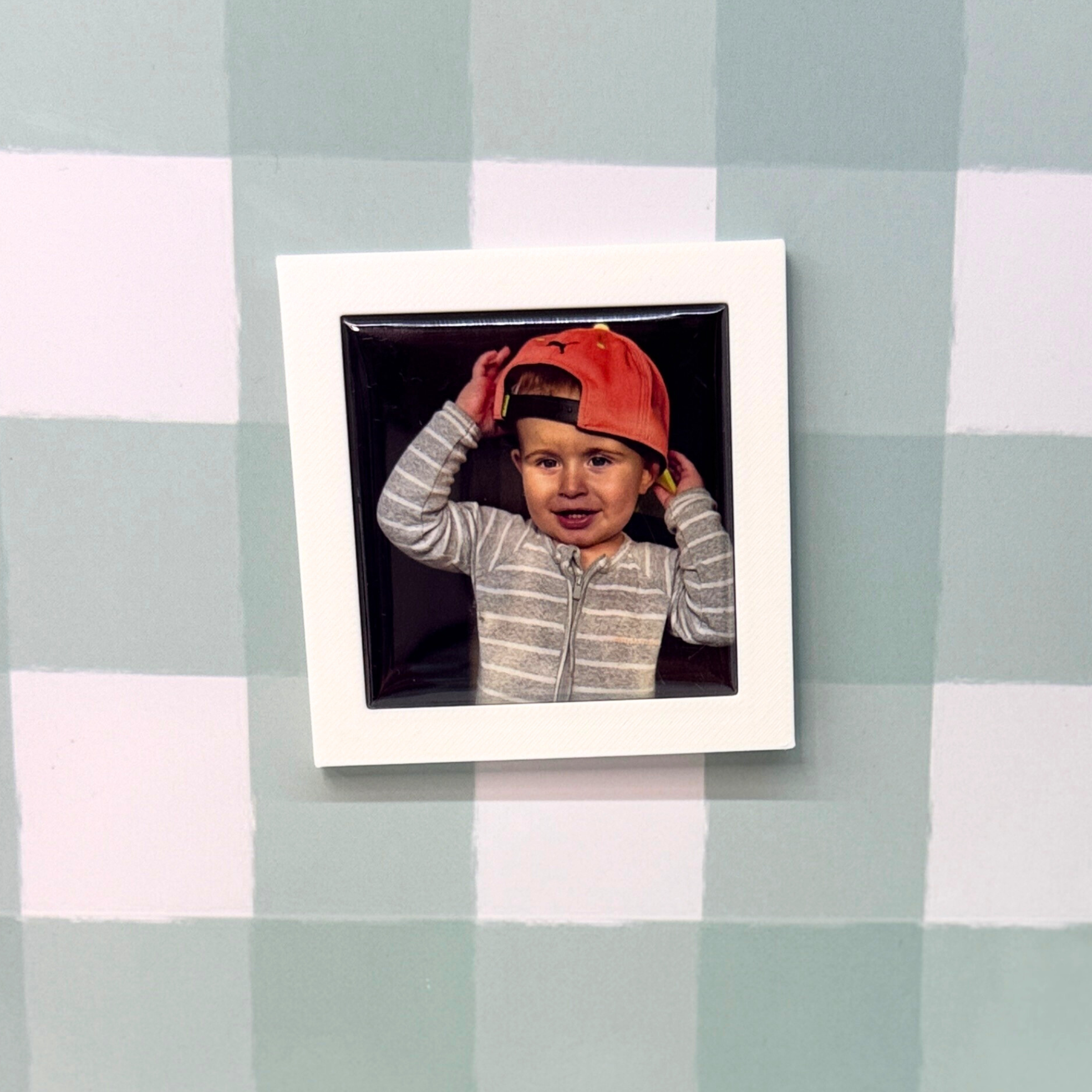 Polaroid photo of a child wearing a red cap on a checkered tablecloth