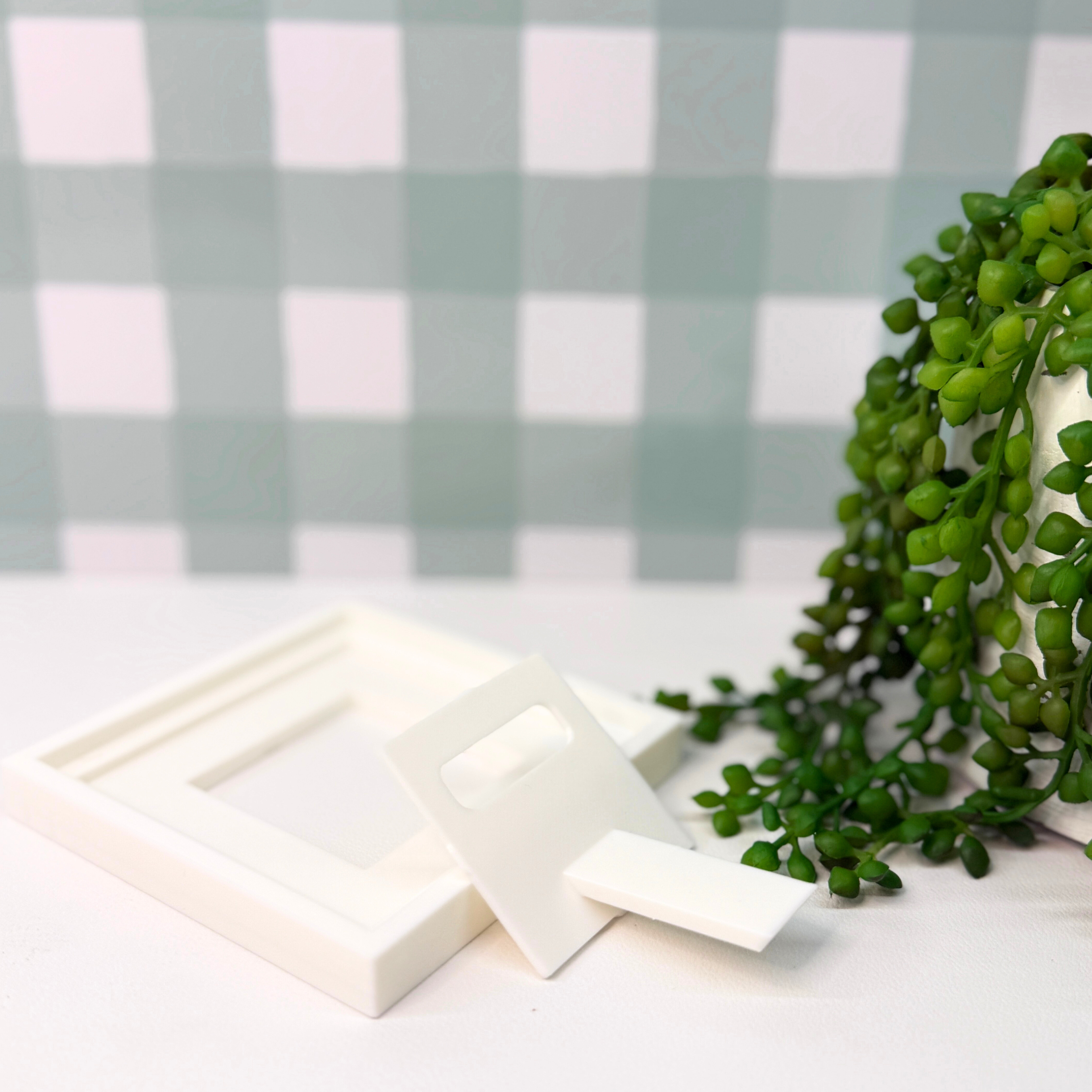 White soap bars on a white surface with greenery and a checkered background