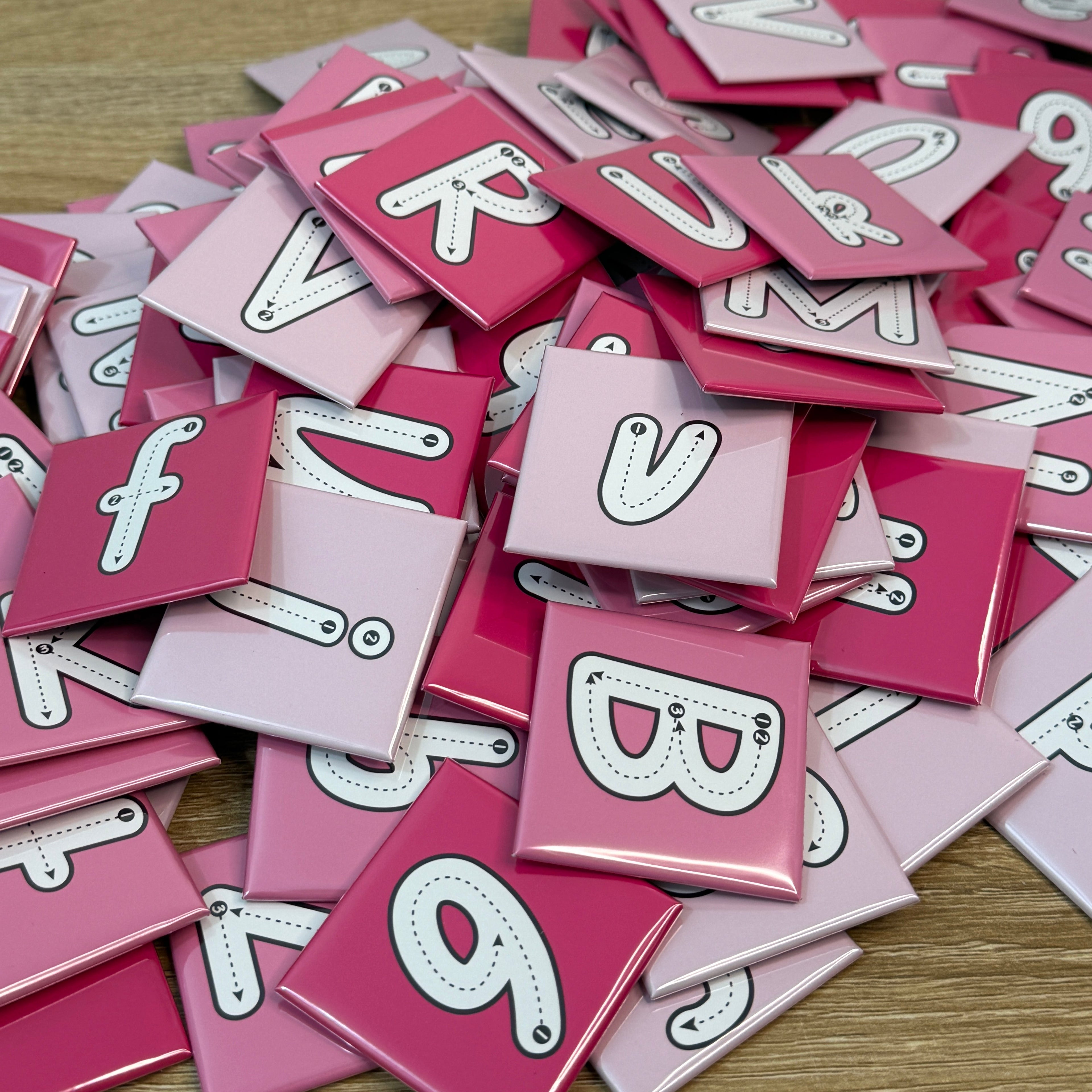 Pile of pink letter tiles with white letters on a wooden surface