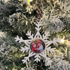 Hand holding a snowflake-shaped Christmas ornament with a bear design against a Christmas tree background.