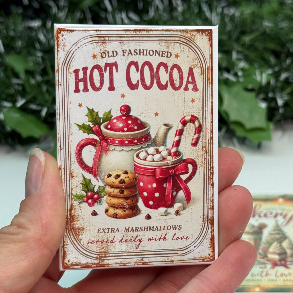 Hand holding a vintage-style 'Hot Cocoa' package with Christmas elements.
