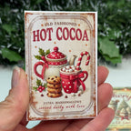 Hand holding a vintage-style 'Hot Cocoa' package with Christmas elements.