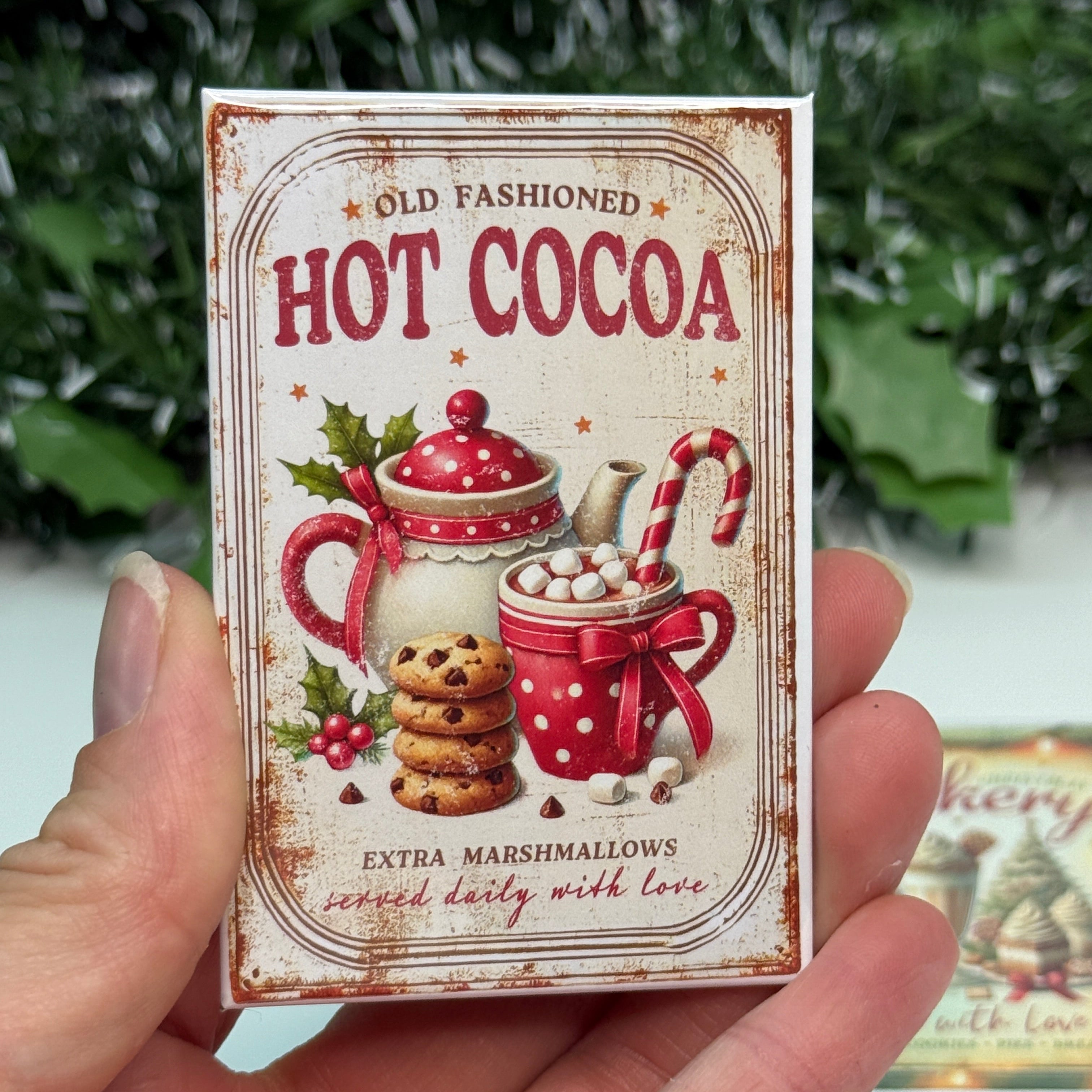 Hand holding a vintage-style 'Hot Cocoa' package with Christmas elements.