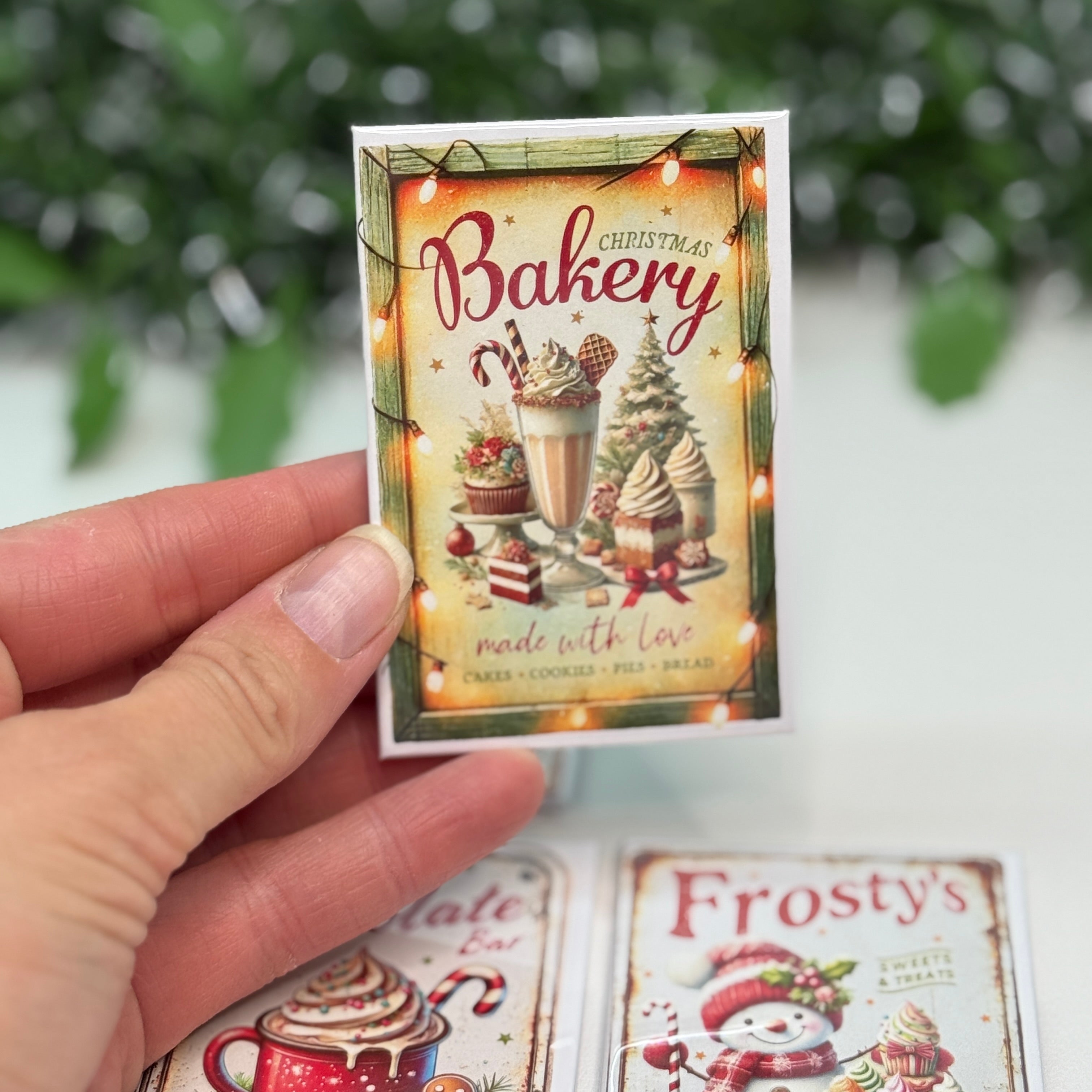 Hand holding a miniature bakery-themed card with Christmas decorations.