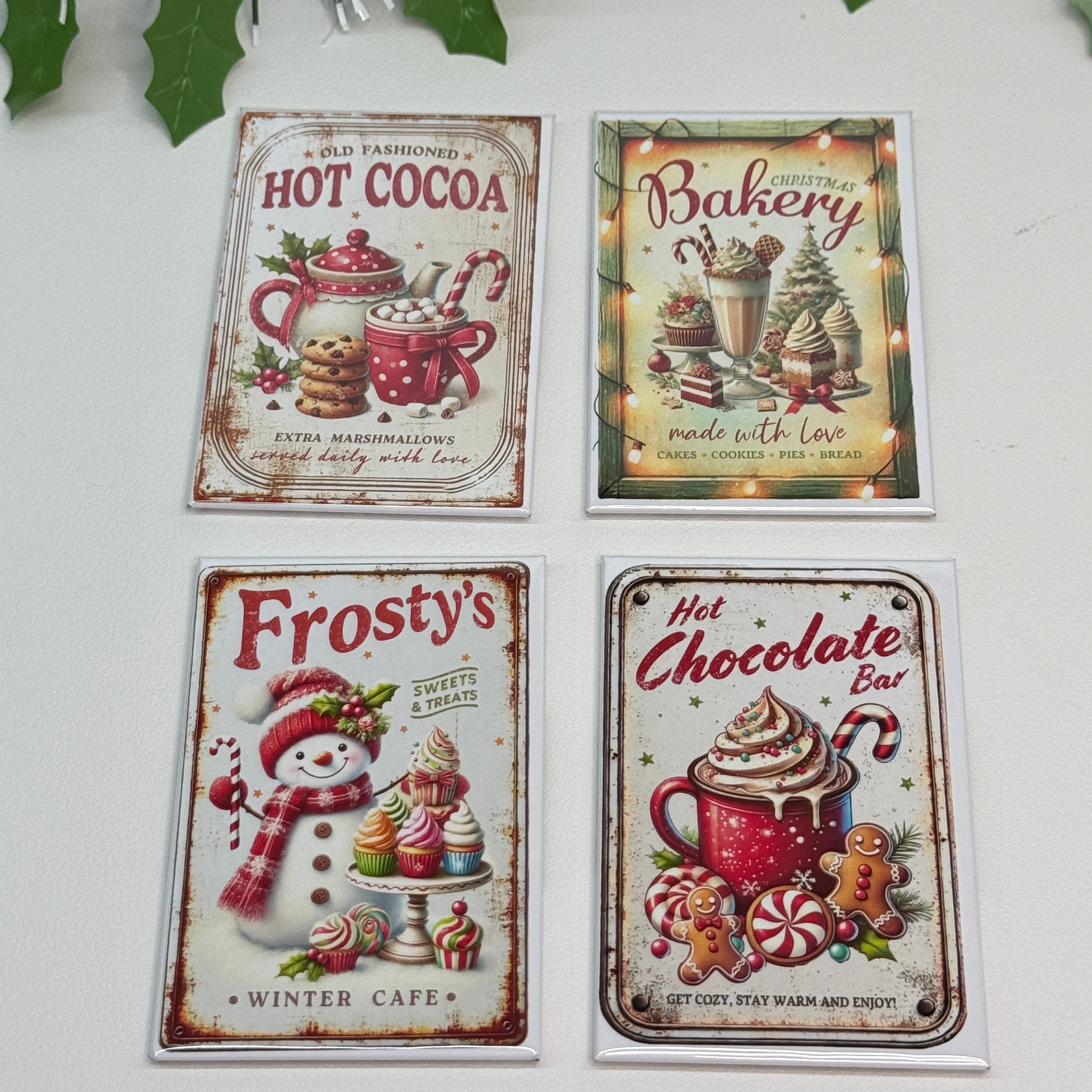 Four vintage-style Christmas-themed metal signs on a white surface with greenery.