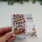 Card with 'In this kitchen we bake with love' text held by a hand on a light background