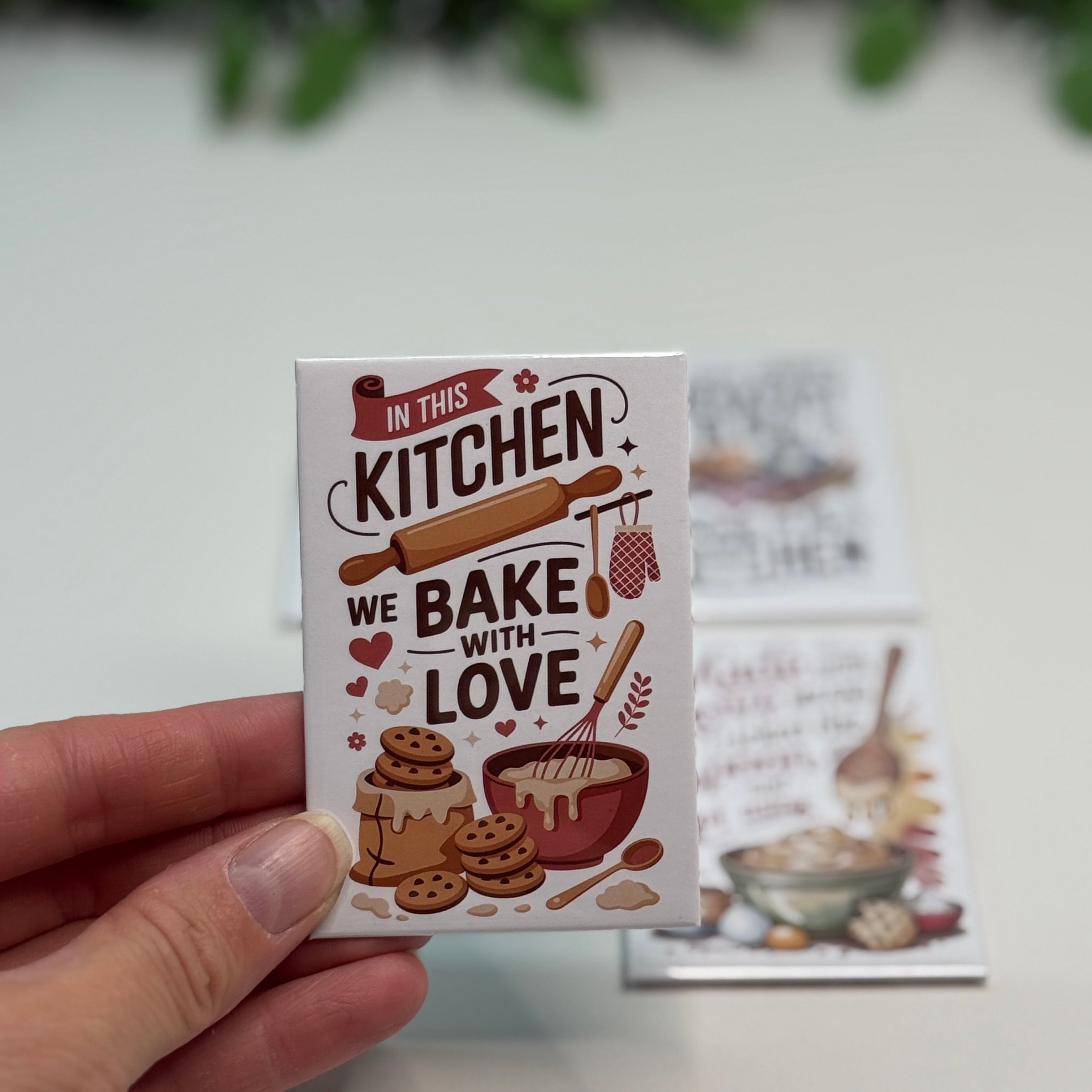 Card with 'In this kitchen we bake with love' text held by a hand on a light background