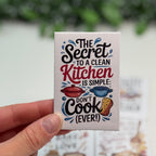 Small card with kitchen-themed text held by a hand against a blurred background