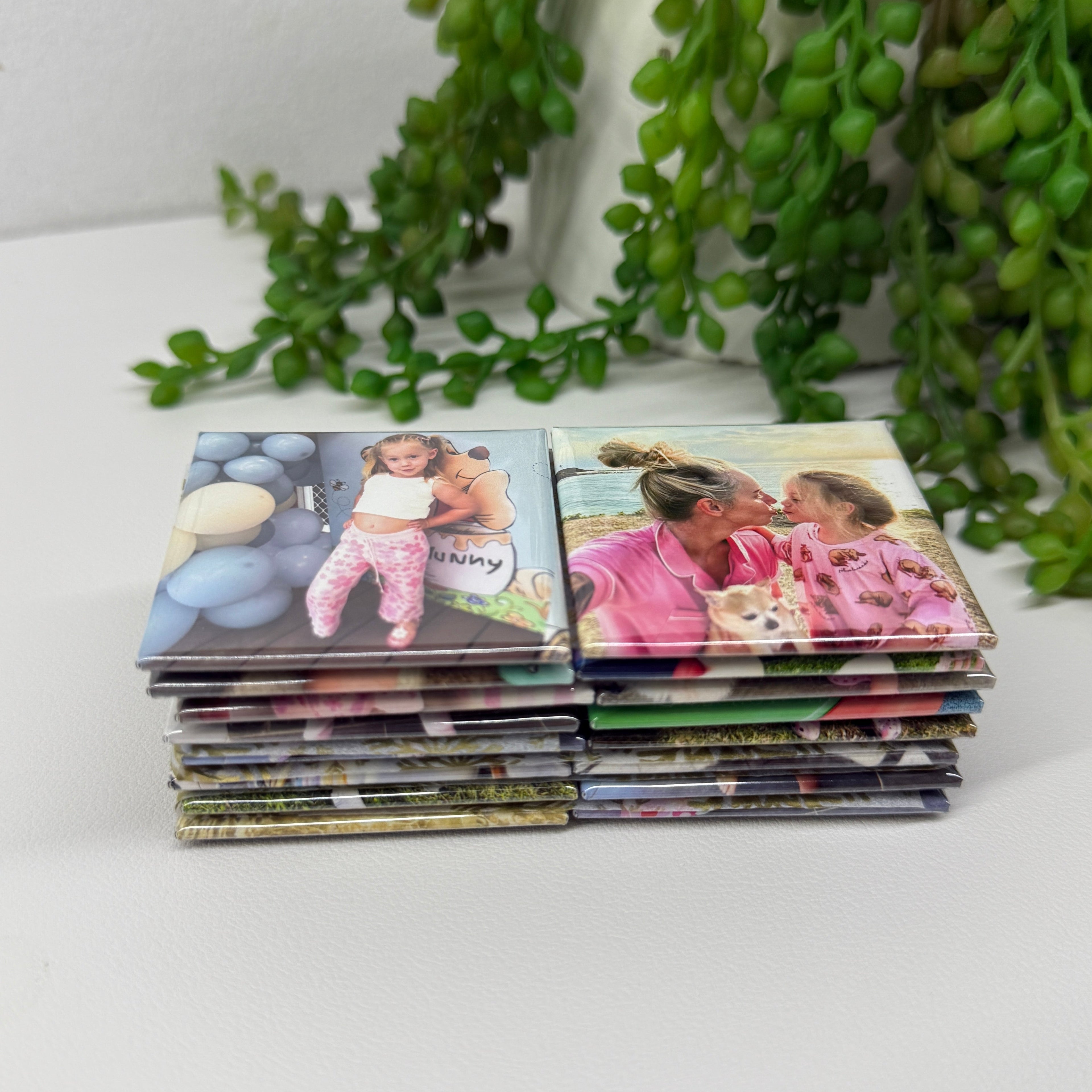 Stack of photo magnets on a white surface with green plants in the background