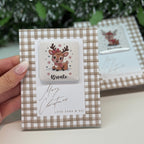 Small decorative box with a reindeer design and 'Bronte' text, held by a hand with a blurred green plant background.