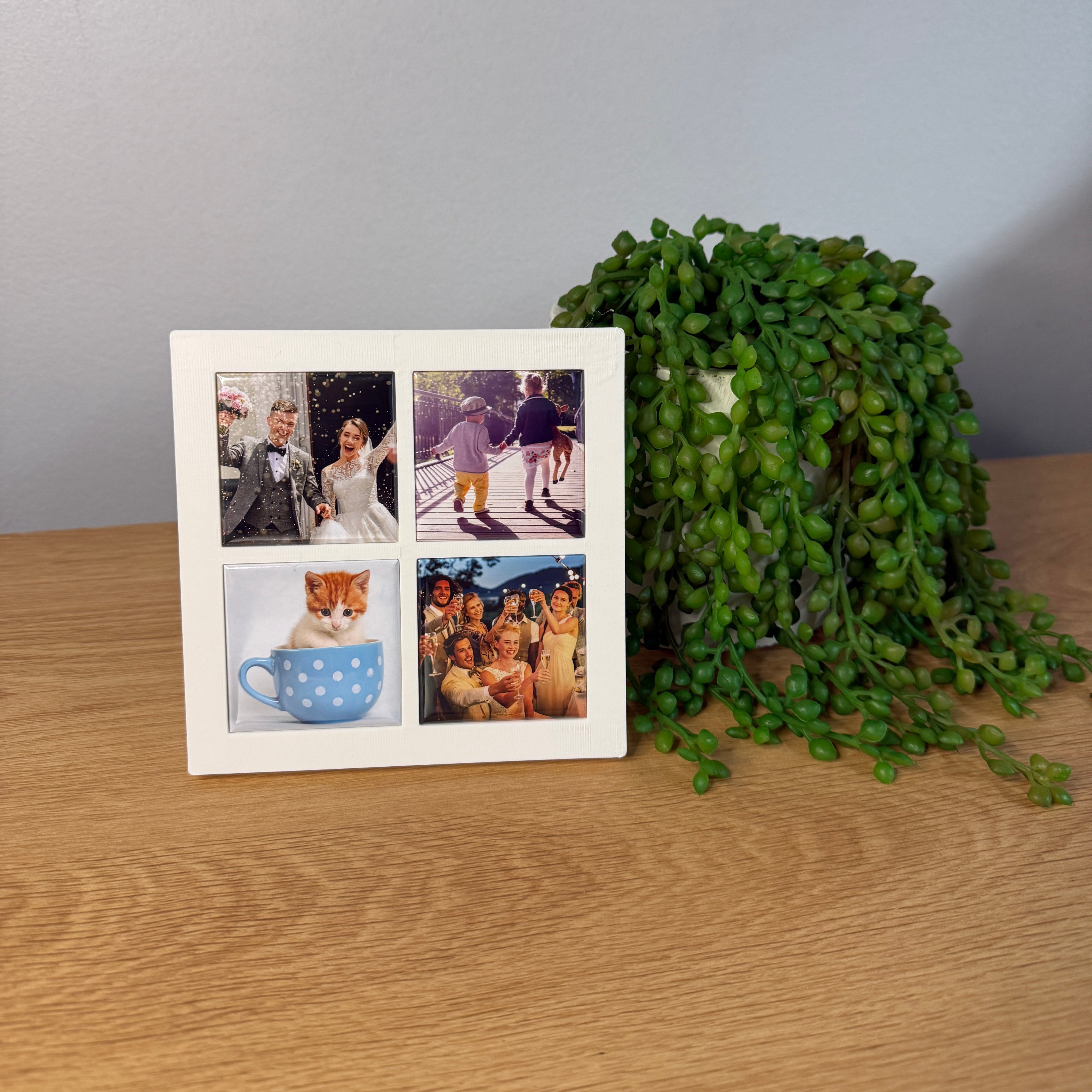 A square white photo collage print with four small printed images, placed on a light wood surface next to a green trailing succulent plant.