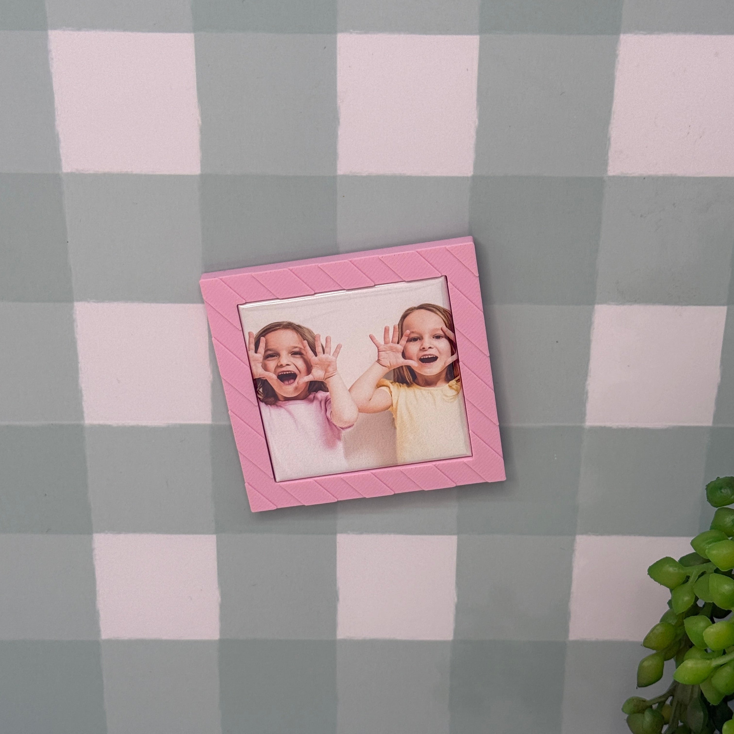 Small pink picture frame with a photo of two children on a checkered tablecloth.