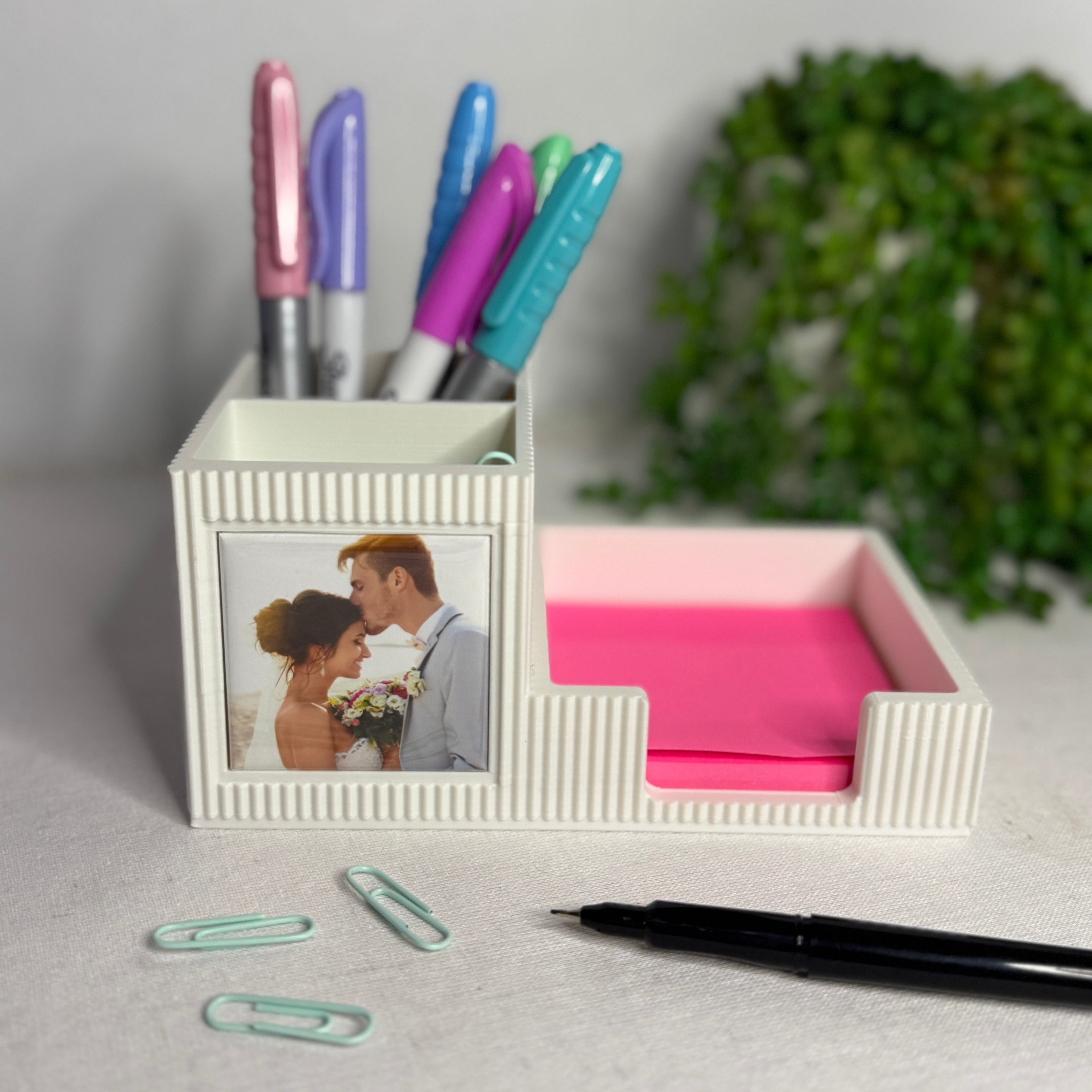 Desk organizer with pens, a photo frame, and a pink compartment on a light surface.