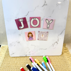 Decorative tiles spelling 'JOY' on a marble surface with markers below.