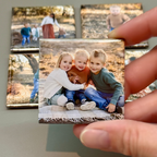 Hand holding a small photo print of three children sitting together, with more photo prints in the background.