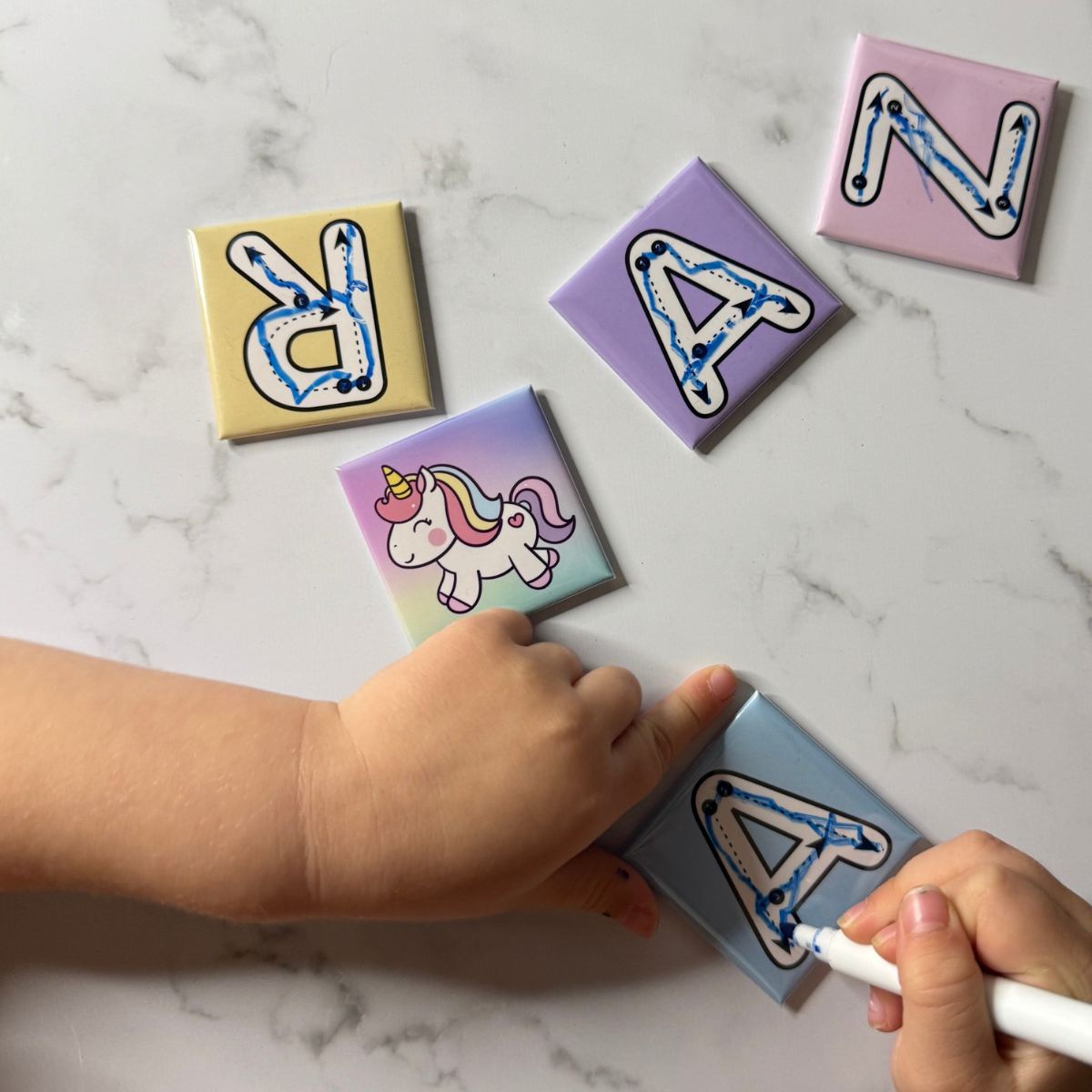 Children's letter tiles with a hand holding a marker on a marble surface