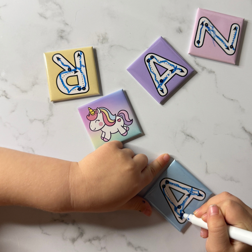 Children's letter tiles with a hand holding a marker on a marble surface