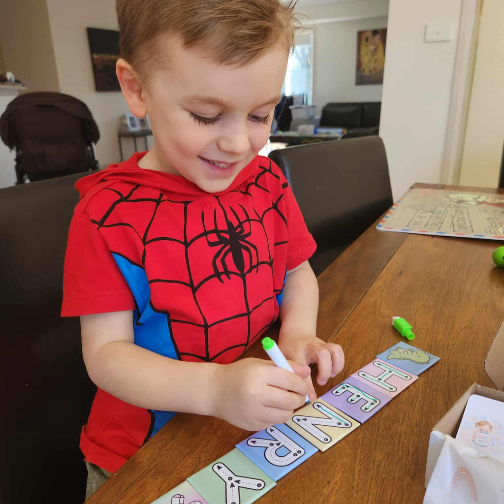 Young boy practising handwriting with Zara’s World write and wipe magnetic letter tiles on a table, smiling while tracing colourful alphabet magnets.